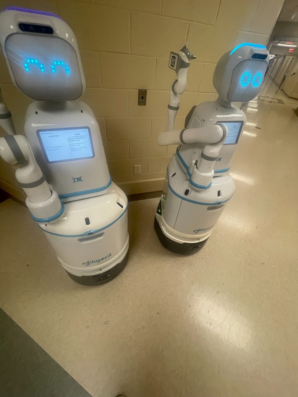 Two Moxi hospital robots waiting in a clinical corridor